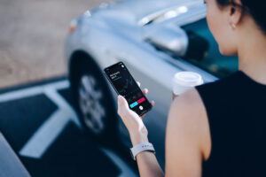Over the shoulder view of young Asian businesswoman having coffee to go, checking financial stock market analysis on smartphone while walking to her car in carpark in downtown district in the city. Business on the go and technology concept